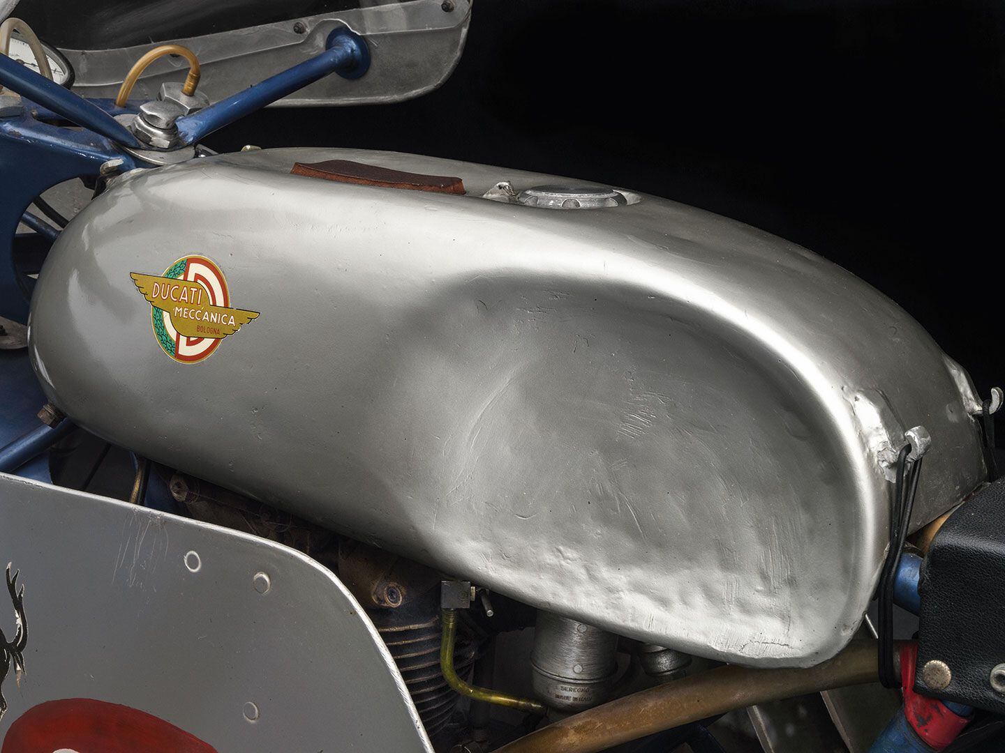 The hand-beaten aluminum tank on a 1959 Ducati 125 Desmo Barcone Grand Prix Racer held in place with rubber bands.