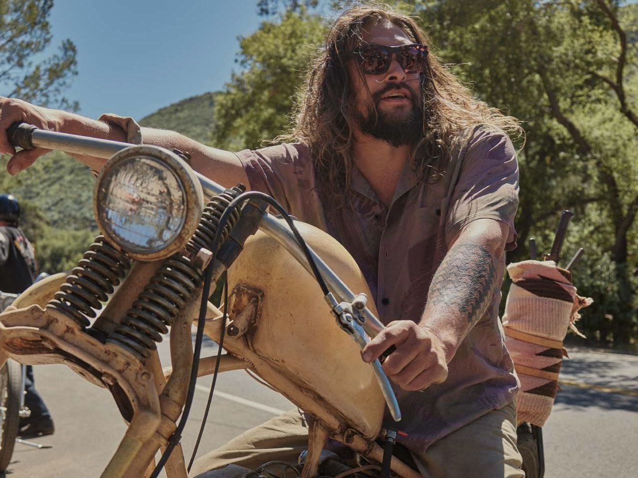 Jason Momoa posing aboard an Ironhead with a springer front end and peanut tank.